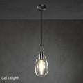 A gold-colored metal pendant light with a clear glass shade, suspended by a chain, against a dark background.