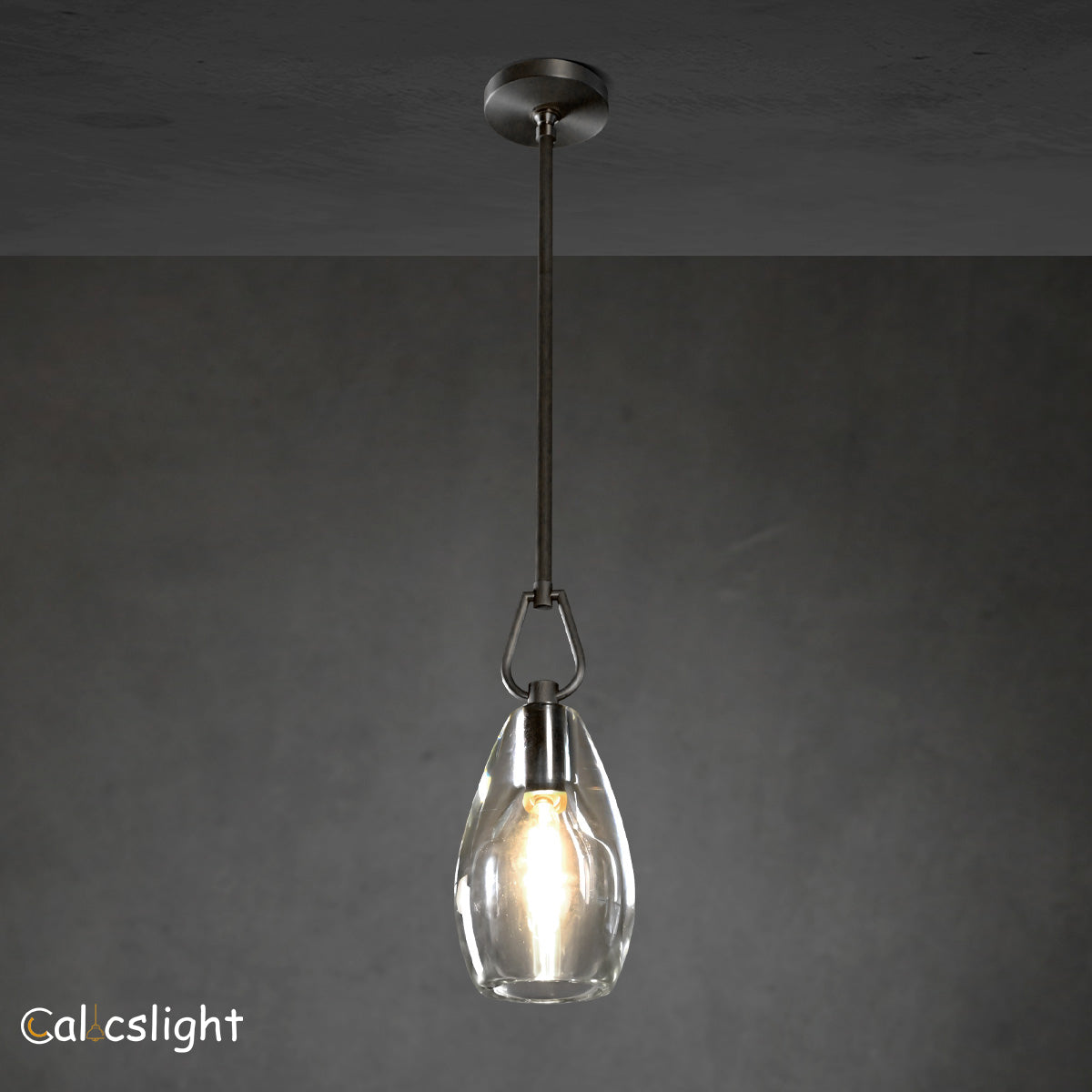 A gold-colored metal pendant light with a clear glass shade, suspended by a chain, against a dark background.