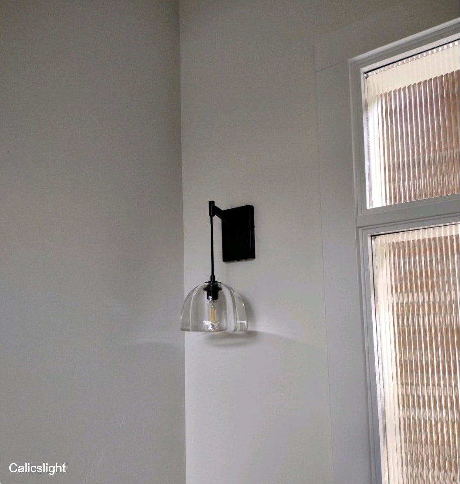 Modern wall-mounted light fixture on a white wall with a window in the background.